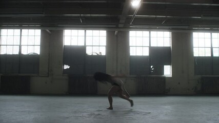Beautiful dancer performs a contemporary dance in an industrial warehouse against the backdrop of large windows