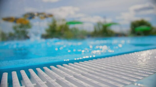 Jump into the pool, splash water into the camera. Blurred background in the foreground is a girl's leg . Slow motion, the concept of a Sunny summer beach and pool, party..