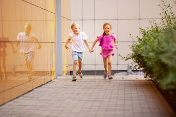 Future. Two smiling kids, boy and girl running together in town, city in summer day. Concept of childhood, happiness, sincere emotions, carefree lifestyle. Little caucasian models in bright clothes.