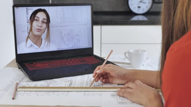 Female makes student conference video call on laptop computer talks with web student, online teacher in remote webcam chat on screen. Distance education s concept. Architect's desk: drawings, tape rul