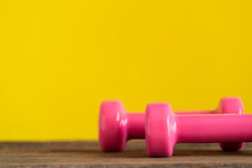 Obraz na płótnie Canvas two pink dumbbell on a wooden table with yellow background, sport and healthy concept