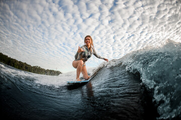 cheerful blonde woman riding down the wave on wakesurf board