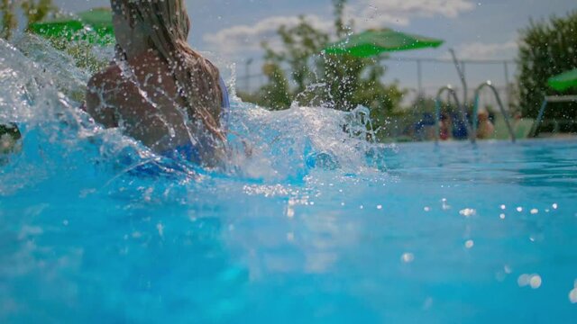 A girl in a swimsuit jumps into the water , a young woman dives into the pool on the street, slow-motion