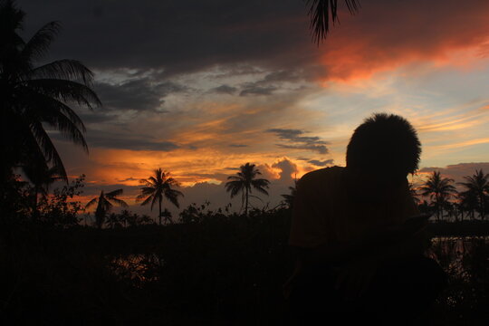 This a images silhouettes of humans and coconut trees in a beautiful sunset