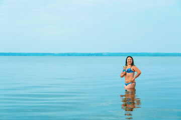 A brunette woman in a swimsuit at dawn in the azure water near the shore.