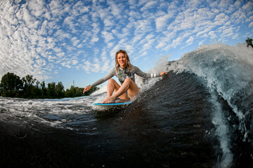 handsome blond woman riding the waves while sitting on wakesurf board