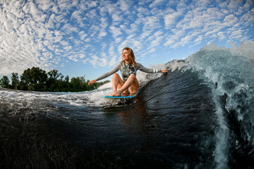happy blond woman riding the waves while sitting on wakesurf board