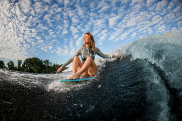 cheerful blond woman riding the waves while sitting on wakesurf board