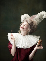 In love with chocolate. Young woman as Marie Antoinette isolated on dark green background. Retro...