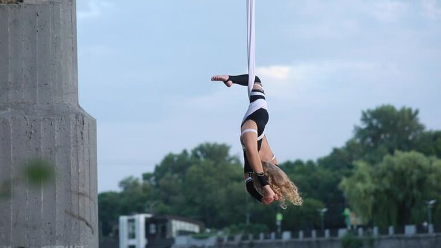 Child girl aerialist performs acrobatic elements and spins in hanging aerial silk.