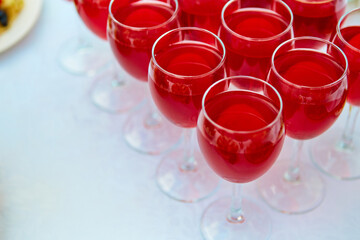 A row of glasses with red drinks, juice, champagne or wine at a party. Catering. Glassware on the table with a white tablecloth. Festive buffet for the holiday.