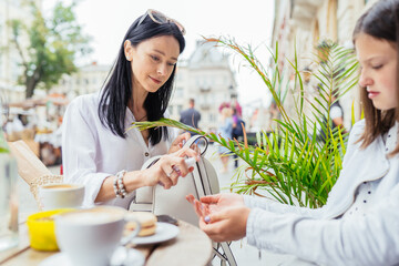 Female using an antibacterial antiseptic to disinfect hands her grow up teenager daughter during they are relaxing at city outdoor cafe. New social rules after pandemic concept.