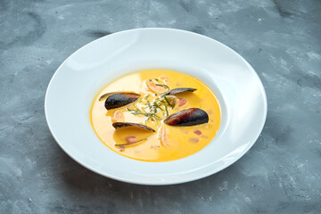 French cream soup bisque with seafood in white plate on gray background