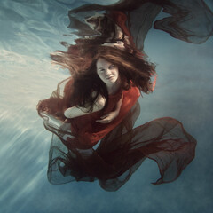 Girl in a red dress with a cloth swims underwater
