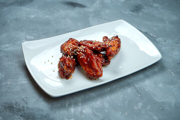 Chicken wings in barbecue sauce with sesame seeds in a white plate on a gray background. Beer snack