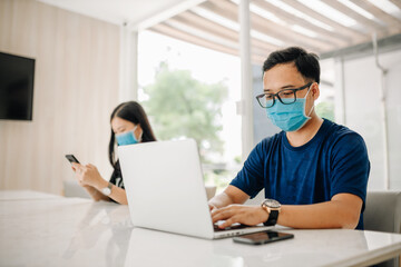Fototapeta premium Asian man wearing a mask and using computer laptop in office or classroom for prevention COVID-19 Virus.