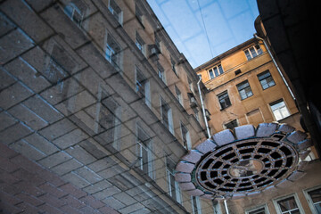 Vintage yellow apartment house reflected in a puddle with manhole