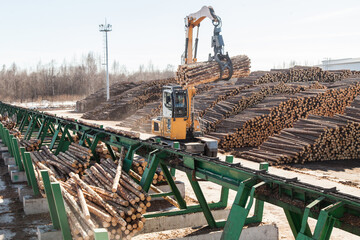 An industrial loader loads logs into a conveyor at a sawmill