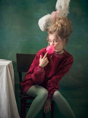 Bubble gum blowing. Young woman as Marie Antoinette on dark green background. Retro style, comparison of eras concept. Beautiful female model like classic historical character, old-fashioned.
