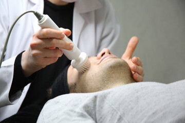 Obraz na płótnie Canvas Professional beautician is rejuvenating male face by cavitation laser apparatus. Man is lying on massage table and relaxing