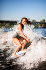cheerful woman wakesurfer actively balancing on surfboard along the wave.