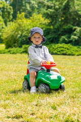 Child playing on green car on green meadow with copy space during sunny summer day