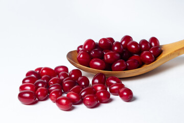 Dogwood on a white background. A wooden spoon full of ripe red dogwood. Not many dogwoods are near. Gathering the summer harvest.