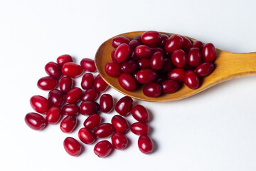 Dogwood on a white background. A wooden spoon full of ripe red dogwood. Not many dogwoods are near. Gathering the summer harvest.
