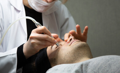 Professional beautician is rejuvenating male face by cavitation laser apparatus. Man is lying on...