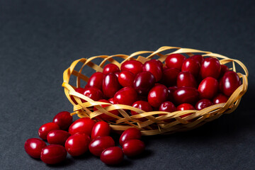 Dogwood on a black background. Wicker basket full of ripe red dogwood. Not many dogwoods are near. Gathering the summer harvest.