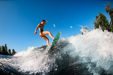 young wet woman energetically balancing on wave on wakesurf board - obrazy, fototapety, plakaty