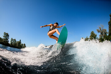 young wet woman energetically balancing on wave on wakesurf board