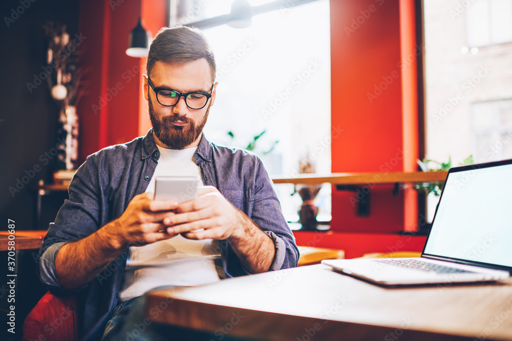 Poster serious male blogger in eyewear for vision correction reading sms with notification for app on smart