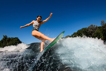Side view of sporty woman who rides the wave on surfboard