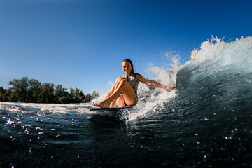happy woman sits on wakesurf board and rides the wave and touches the waves with one hand