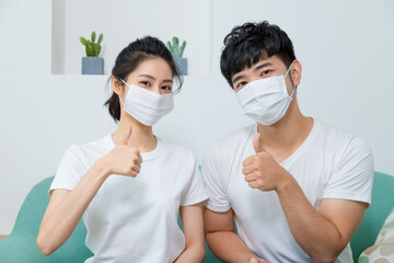 Asian couple wearing protective face mask and showing thumb up at home.