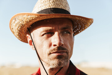 Image of unshaven adult man looking aside while standing at cereal field