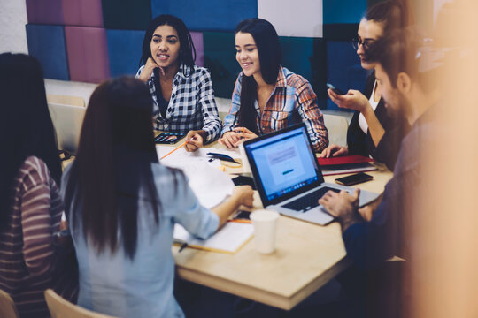 Crew of International  talented students making research in websites on laptop with blank screen and sharing coursework details,male and female architects creating new blueprints for office building