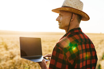 Image of adult man working with laptop while standing at cereal field
