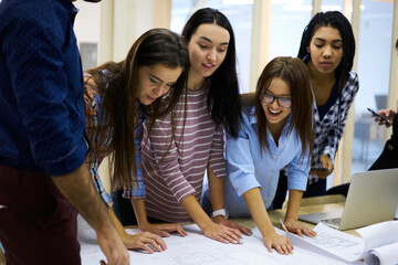 Group of diversity male and female students making preparation for university seminar while talking in friendly atmosphere,professional colleagues checking sketches standing in coworking space