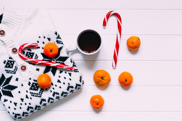 Fototapeta na wymiar top view of knitted sweater, candy, tangerines and a cup of hot
