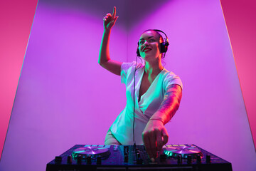 Summertime. Young female musician in headphones performing on purple background in neon light. Concept of music, hobby, festival, entertainment, emotions. Joyful party host, DJ, portrait of artist.
