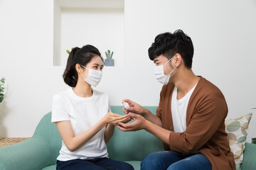 Asian couple using sanitizer alcohol gel to washing hand each other for prevent coronavirus or covid 19 in living room.