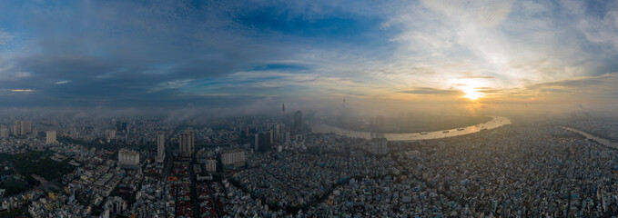Aerial panorama of colorful sunrise and morning fog in Ho Chi Minh City featuring the Saigon River and landmark high rise buildings obscured by low cloud