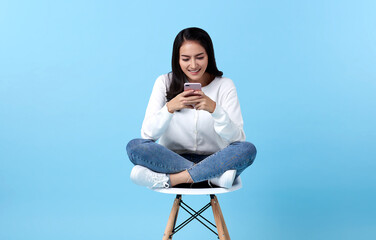 Young woman asian happy smiling while her using smartphone on white chair isolate on bright blue...