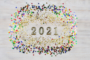 Golden numbers 2021 surrounded by gold and colored stars on a light wooden background. The symbol of the new year. New Years Celebration 2021.