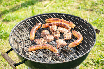 Grilling pig meat and sausages for a campfire party.