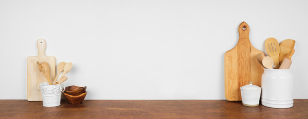 Kitchenware and utensils on a wooden shelf or counter. Banner with  copy space against a white wall. Home kitchen cooking decor.