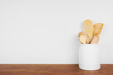 Kitchen cooking utensils on a wooden shelf or counter against a white wall background with copy...