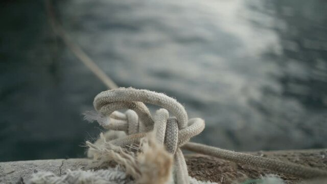 White rope with a knot to tie the boat that is in the port near the sea